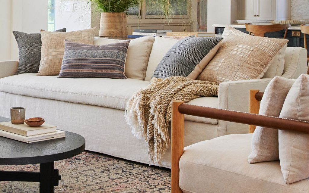 Throw pillows, white slipcover couch, wood armchair, transitional style living room, black coffee table, vintage rug, amber interiors, Anthropologie home, beige throw blanket