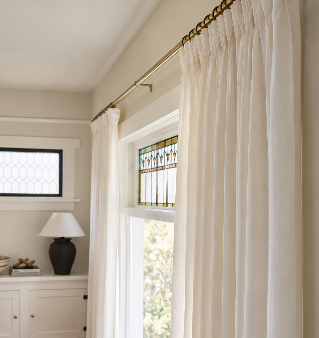 Floor-to-ceiling white pinch-pleat curtains hung from brass curtain rod.